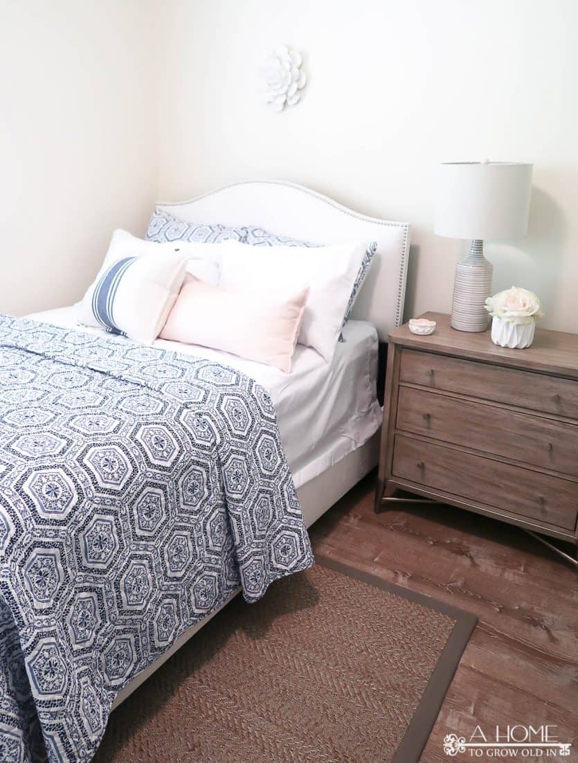white upholstered bed with blue and white patterned quilt and wood nightstand with lamp