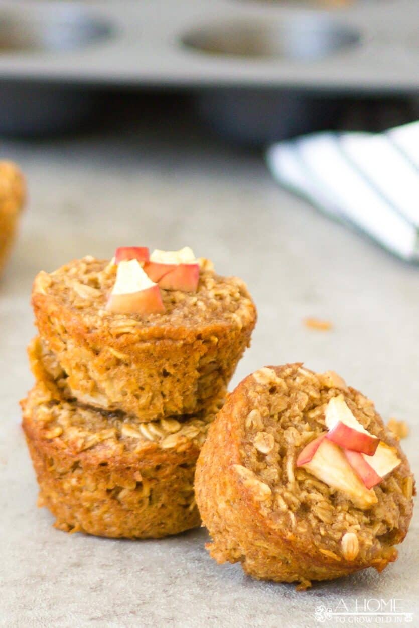 Three cinnamon apple oatmeal muffins with a towel in the background