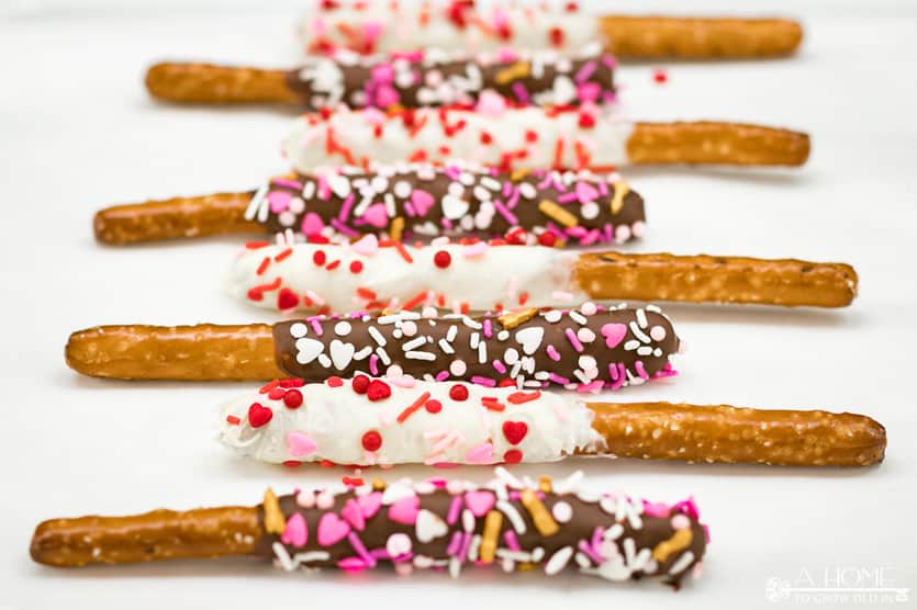 white chocolate and milk chocolate covered pretzel rods with valentines day sprinkles lined up on parchment paper