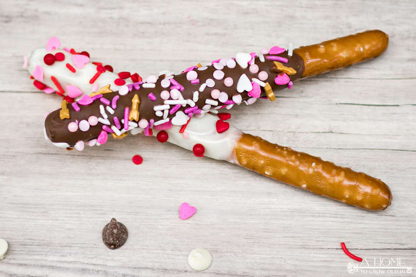 white chocolate and milk chocolate covered pretzel rods with valentines day sprinkles on a wood surface