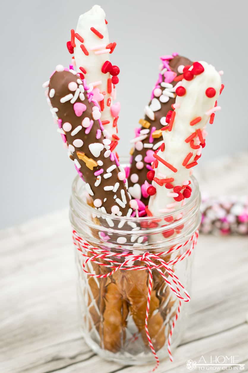 white chocolate and milk chocolate covered pretzel rods with valentines day sprinkles in a mason jar