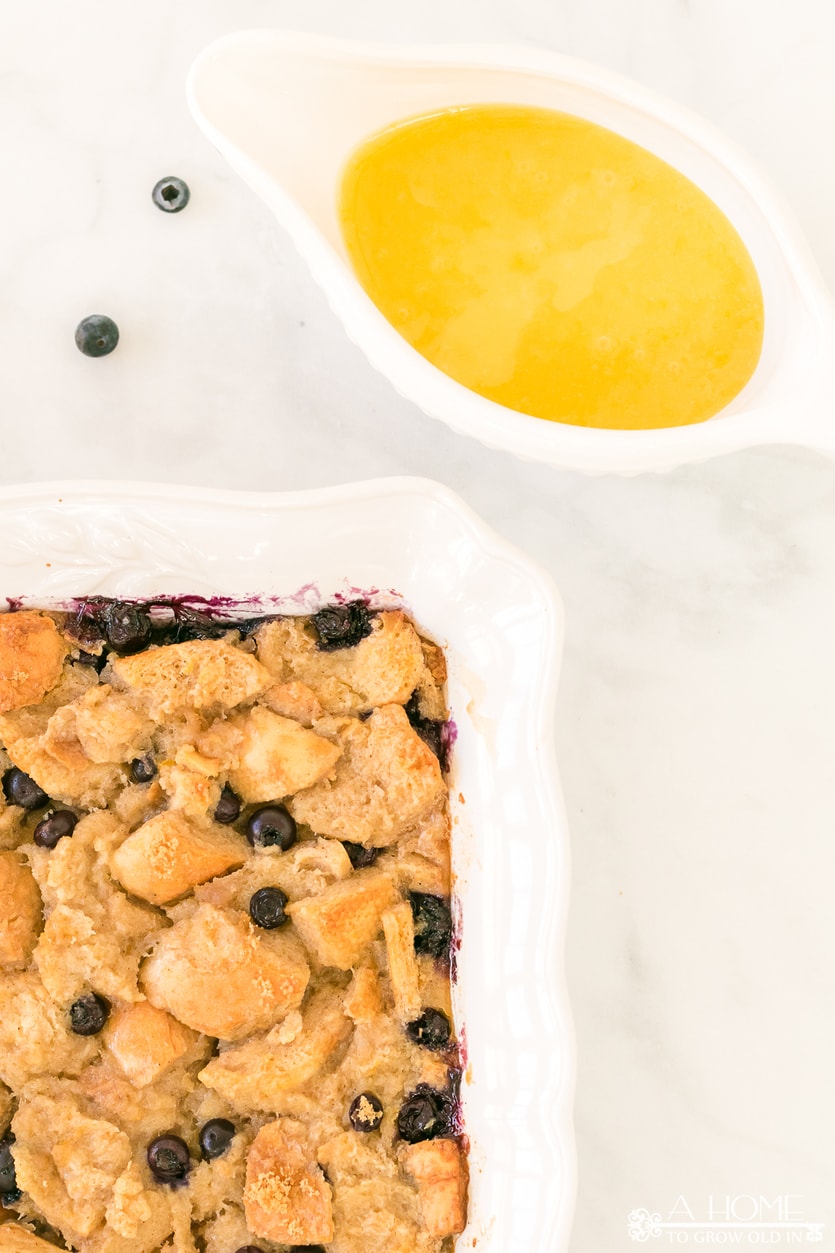 lemon blueberry bread pudding in a baking dish with lemon curd sauce in a pitcher