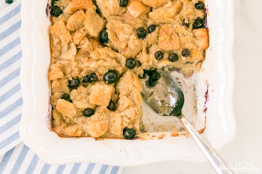lemon blueberry bread pudding in a white baking dish with a portion scooped out